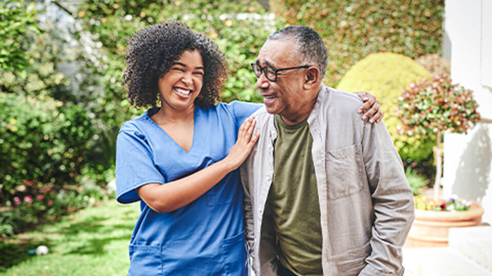 Male senior living resident walking outdoors as his caregiver helps to stabilize him at Traditions of Westfield