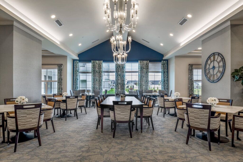 Formal dining room at Traditions of Westfield with chandeliers, vaulted blue accent ceiling, and window seating